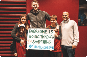 Kevin Love with fans before game, holding Everyone Is Going Through Something sign
